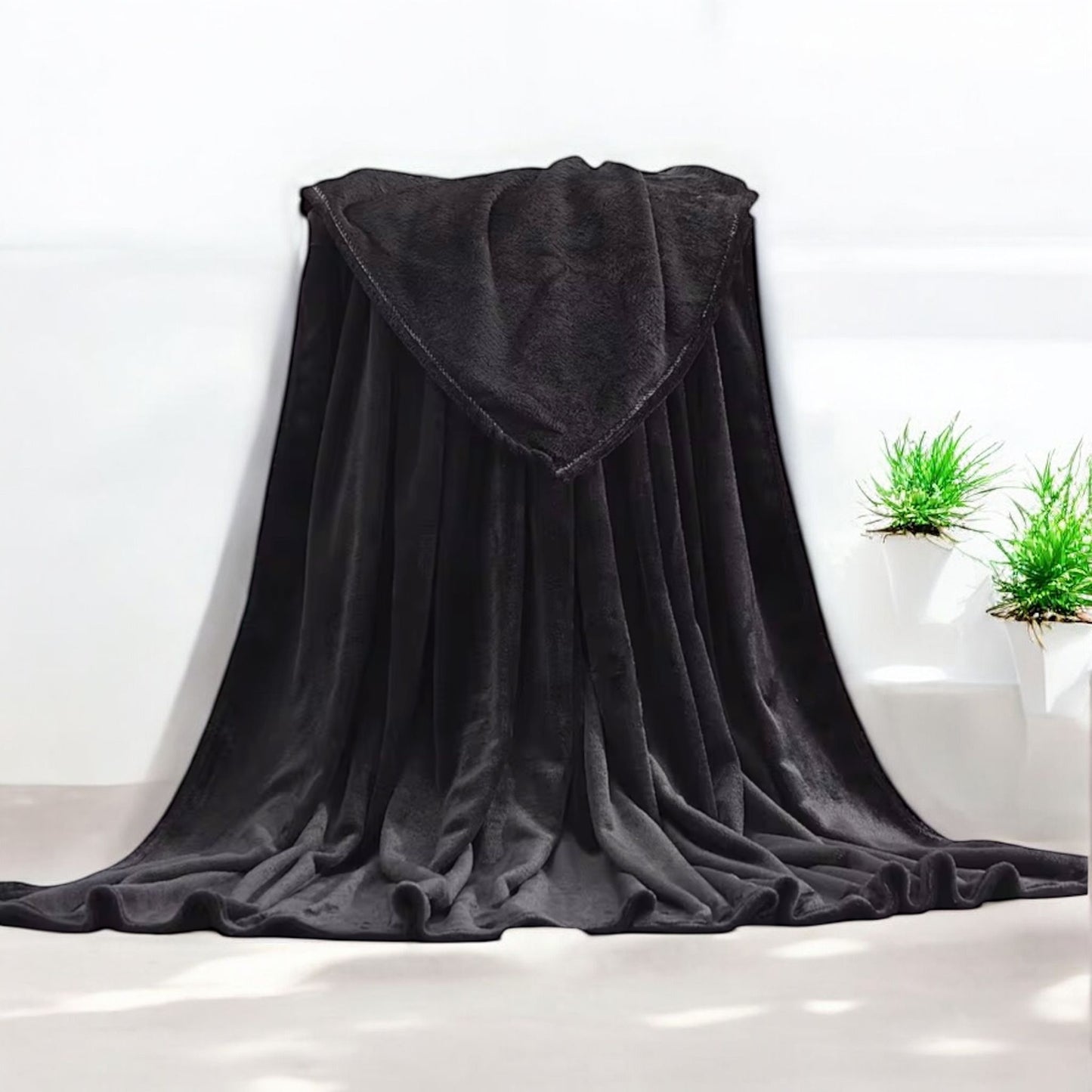 Black blanket draped over a surface with a white background and plants in the corner.