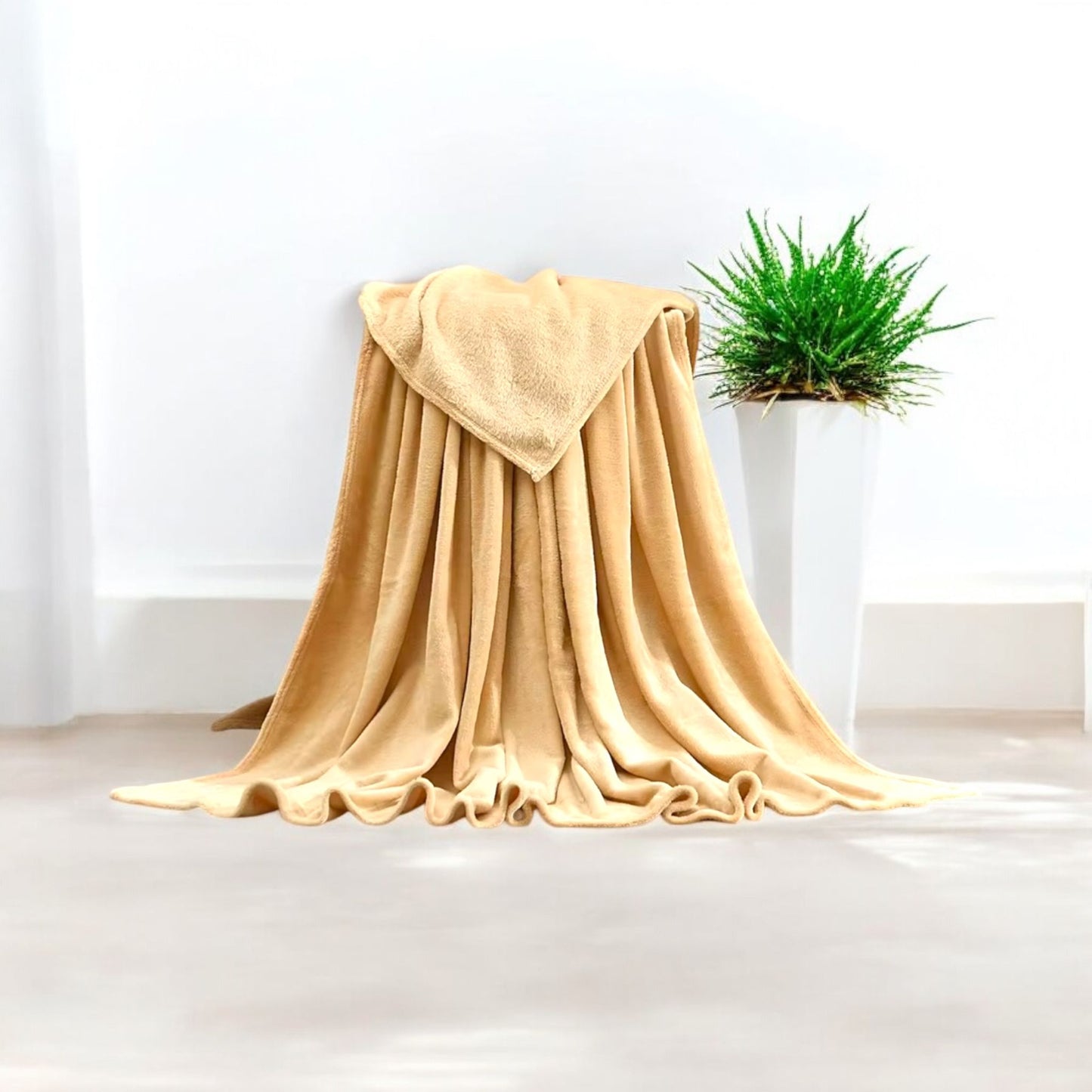 Beige blanket draped over a chair with a plant in the background on a white floor and wall.